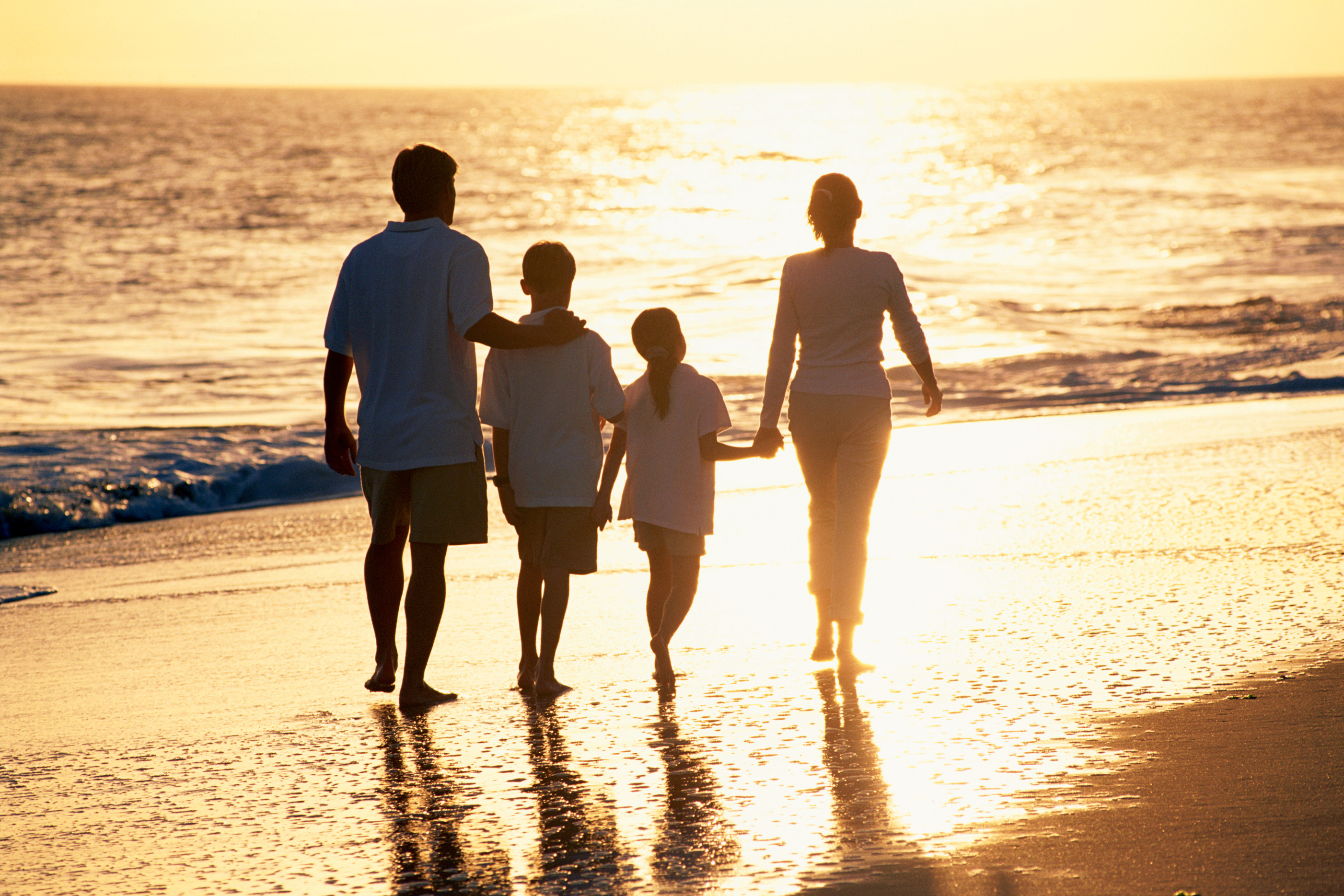Family walking along beach at sunset